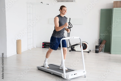 Sporty young man running on treadmill at gym