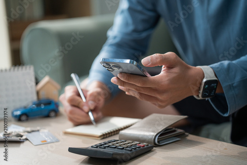 Man hand using smart phone and calculator to manage monthly expenses, saving for house and car, personal finance budget planning concept at home