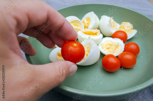 Healthy Snack — Hand Holding Cherry Tomato Over Bowl of Boiled Eggs