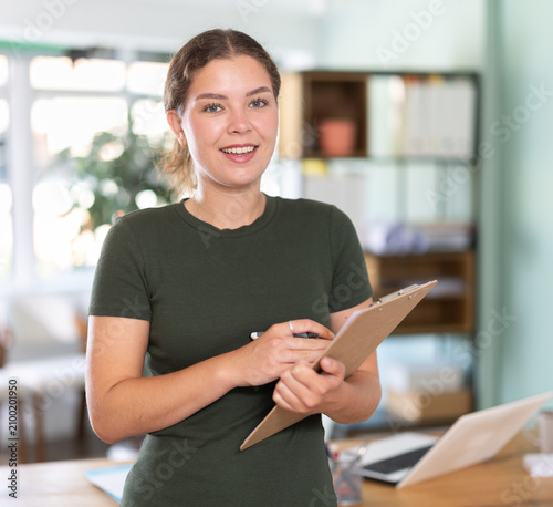 Принти на полотні Young female professional in dress holds clipboard, speaking and conducting surv