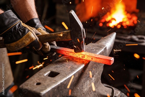 A blacksmith hammers a glowing hot iron bar on an anvil in a workshop with sparks flying around.