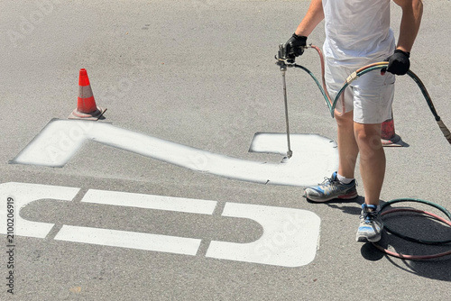 Municipal worker applying a speed limit 20 road marking on asphalt pavement. Concept of traffic regulation, road safety, urban infrastructure, transportation and public services