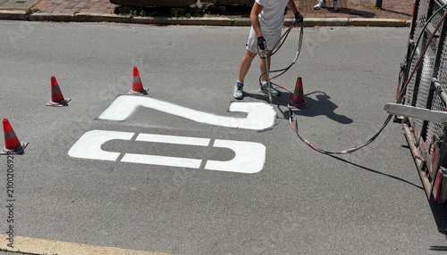 Municipal worker applying a speed limit 20 road marking on asphalt pavement. Concept of traffic regulation, road safety, urban infrastructure, transportation and public services