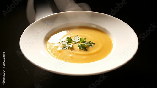 Steaming Bowl Of Gourmet Soup With Fresh Herbs Served In White Dish Against Dark Background