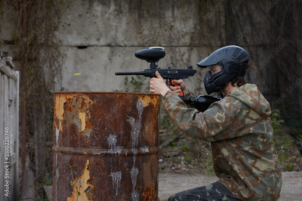 Fototapeta premium A soldier aims a gun while leaning on a drum, hiding behind