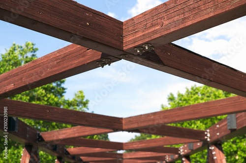 Selective focus. Open timber frame pergola structure with wooden beams showing empty gaps to the blue sky