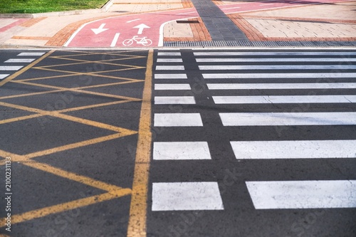 Selective focus. Modern urban road marking with white pedestrian zebra crossing yellow box junction and red asphalt bike lane