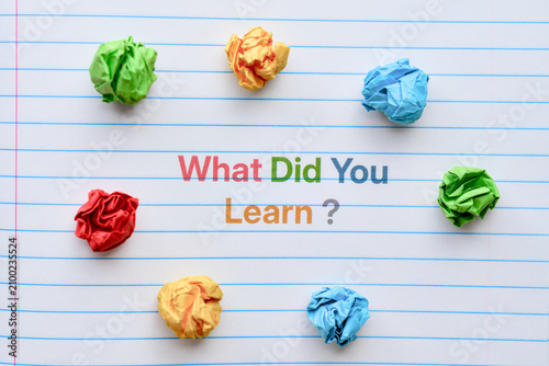 A lined notebook page featuring the question What Did You Learn? printed in colorful letters, surrounded by crumpled paper balls. Close up.