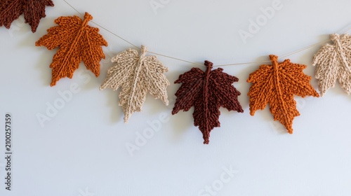 Close up of a knitted autumn maple leaf garland hanging on a white wall.