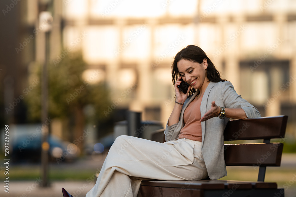 Fototapeta premium Businesswoman talking on phone sitting on park bench