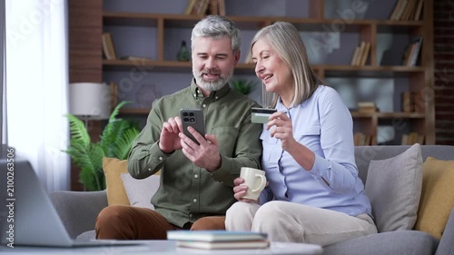 Senior married couple using a mobile phone and credit card for online shopping at home. Retired husband and wife browsing products, making digital purchases and satisfied with their buying decisions.