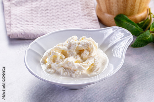 Creamy stracciatella cheese in white ceramic bowl with mint leaves and linen napkin
