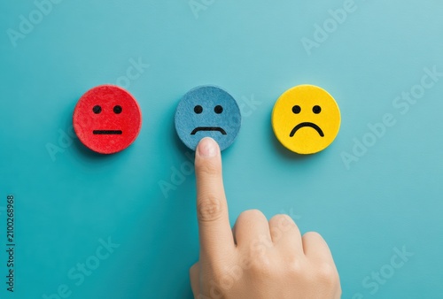 Unhappy Customer Experience: A finger points to a sad face emoji, symbolizing dissatisfaction or a negative customer review, with red and yellow emojis nearby.