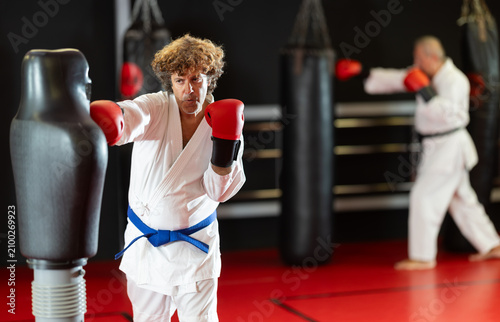 Vászonkép Man in white kimono trains in gym - he punches a sports dummy