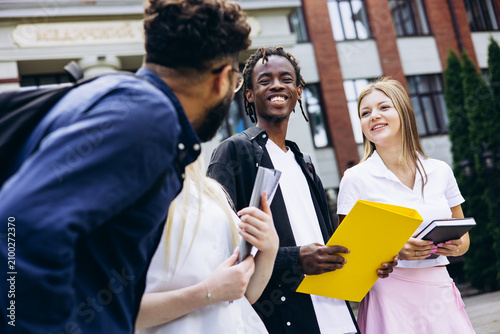 Group of diverse university students sharing a happy moment, smiling and communicating outdoors on campus with books