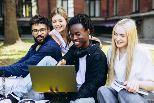 Group of diverse college students studying and working together outdoors on a laptop, sharing ideas and smiling