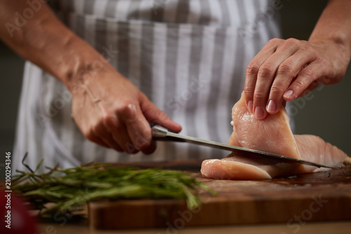 Chef slicing raw chicken breast on wooden board