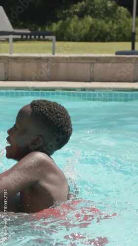 Vertical video: Dad carrying son in red trunks on shoulders, playing in home pool by beach ball