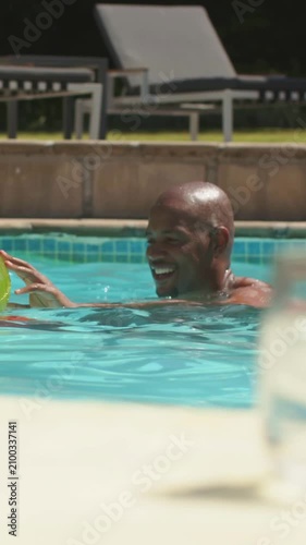 Vertical video: Holding green float, shirtless dad playing with teen at pool, swimming toward glass