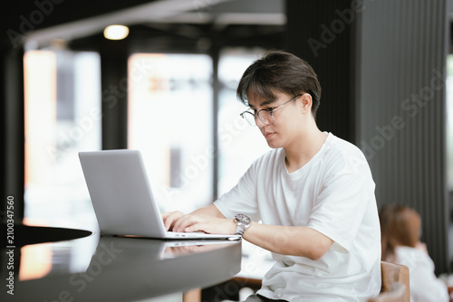 Young professional talking on smartphone while working on a laptop in a modern café, holding a coffee cup with natural window light.