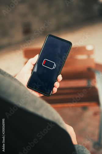 Low battery warning icon on smartphone screen held by mature woman hand. battery anxiety, technology dependency, and power management issues concepts.