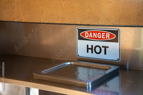 Danger Hot warning sign mounted on a stainless steel bench in a commercial kitchen environment
