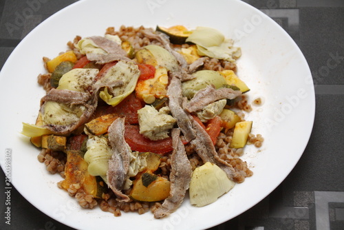 Appetizer, side salad with buckwheat, artichokes, tomatoes, zucchini, anchovies, olive oil, basil, herbs.