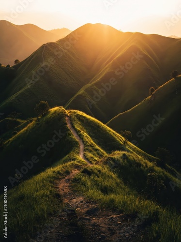 Breathtaking golden hour view of a winding dirt trail leading up misty, grass-covered rolling hills and peaks.