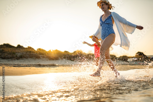 Photos Happy mother and daughter running and splashing through ocean waves during summe
