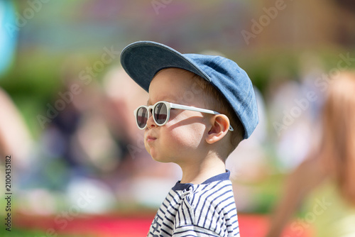 The child, enjoying a sunny day in the fresh air, wears sunglasses and cap during a bright summer event in the park.