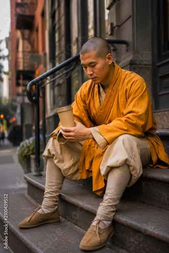 Monk Sitting on Urban Steps Holding Coffee Cup