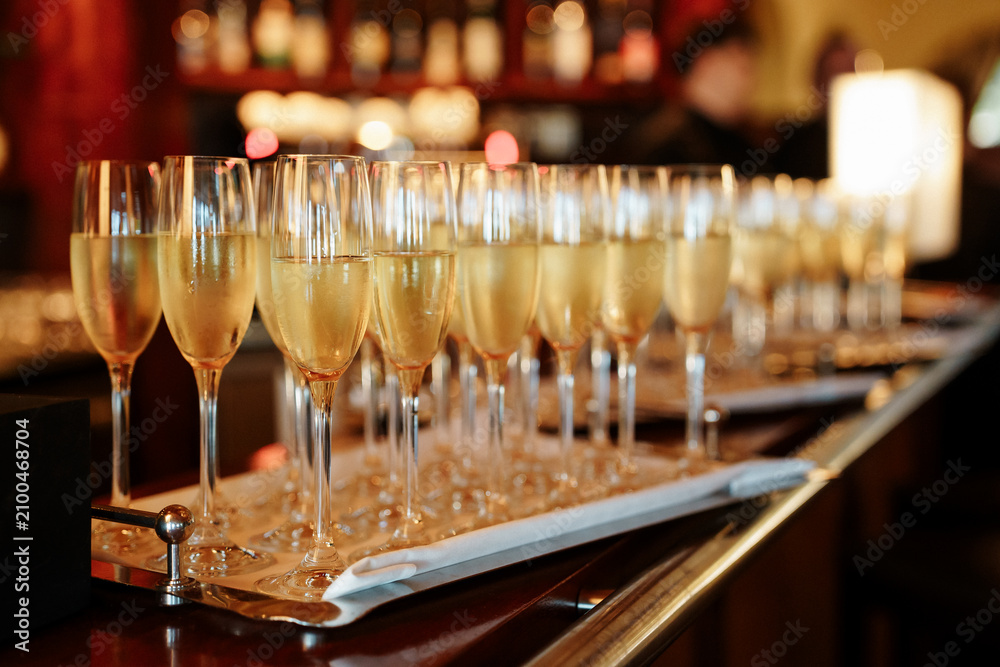 Fototapeta premium Row of champagne flutes filled with sparkling wine on a silver tray, captured in a dim, atmospheric bar setting perfect for events and nightlife, celebrating festivities, events, toast