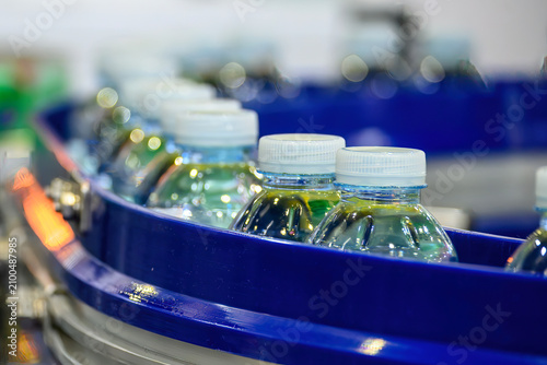 Macro shot of filled drinking water bottles moving on an automated conveyor belt in a bottling plant.