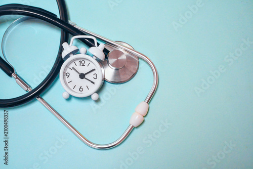 Medical stethoscope and small alarm clock on a blue background