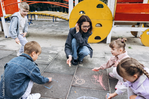 Bild auf Leinwand Positive smiling teacher and young children drawing on playground with chalk