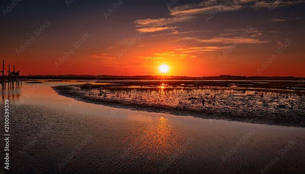 Fototapeta premium Sun Dips Below Horizon Casting Warm Glow On Virginia S Coastal Salt Marsh Water Reflects Fiery Sky Wetland Tidal Marsh