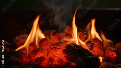 A dynamic video captures flames and glowing embers crackling intensely on a grill in a warm outdoor setting