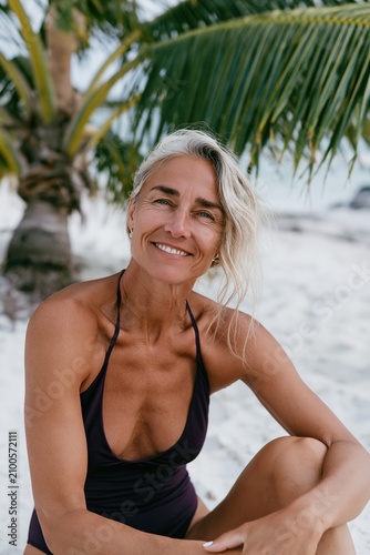 Woman in swimsuit sitting on white sand beach with palm tree for tropical vacation banner and wellness travel background