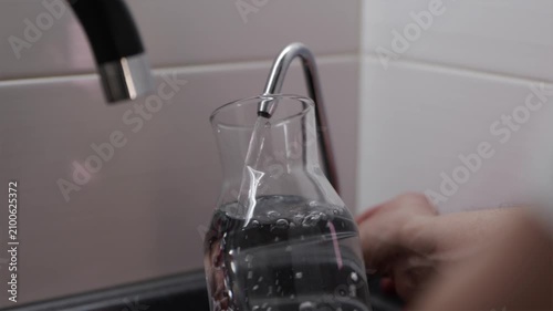 Filling reusable glass bottle with fresh filtered water from kitchen tap