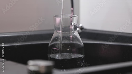 Fresh drinking water pouring from kitchen tap into reusable bottle