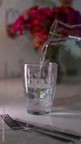Pouring clean water into glass on dinner table vertical