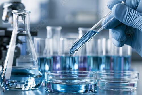 Scientist carefully drops blue liquid from pipette into petri dish in laboratory