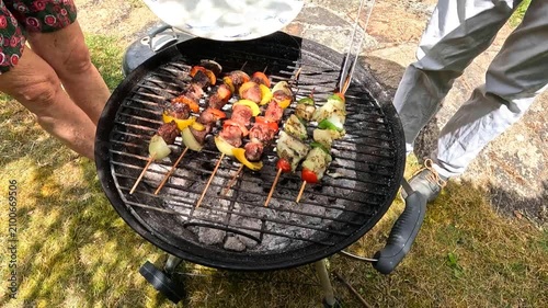 Lifting grilled fish skewers off the charcoal BBQ and serving them on a plate.