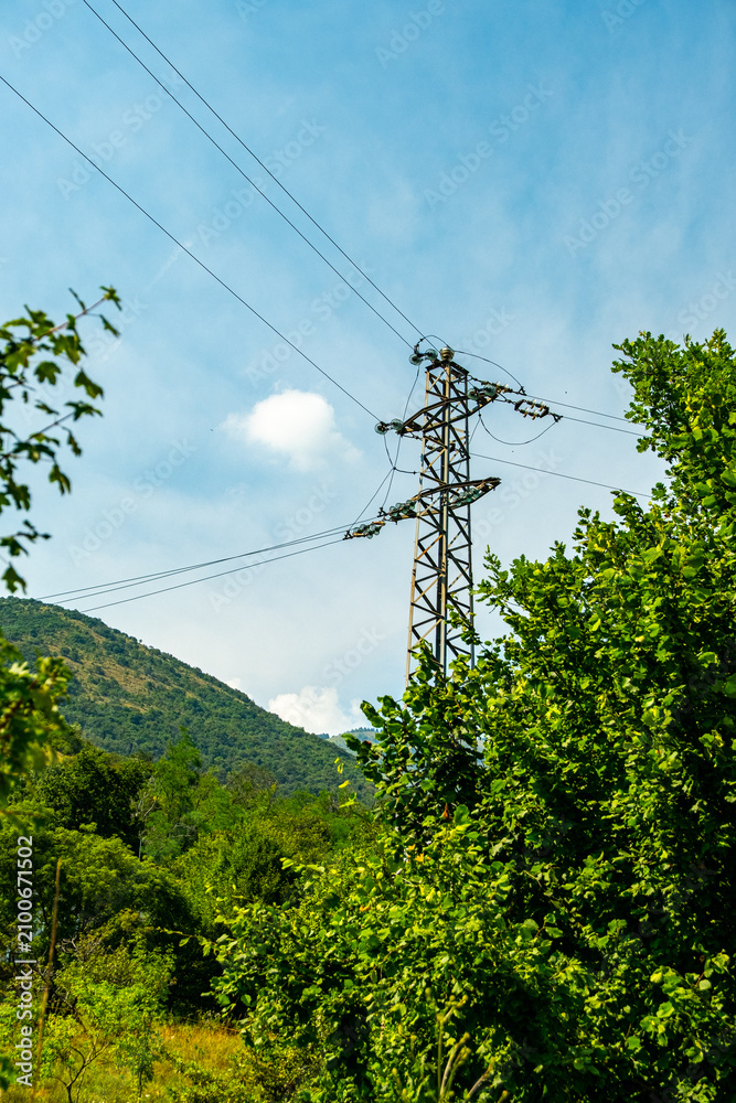 Fototapeta premium High-voltage transmission tower surrounded by forested mountains in northern Italy