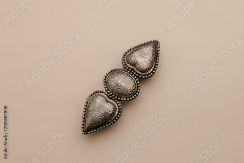 Konstfotografi Ornate Silver Metal Accessory with Three Heart-Shaped Elements on a Cream Backgr