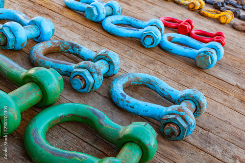 Row of heavy duty industrial colorful steel lifting shackles laid out on a ship wooden deck surface