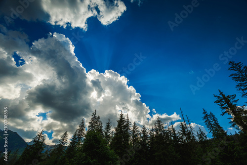 Dramatic blue sky with sun rays shining through fluffy white clouds