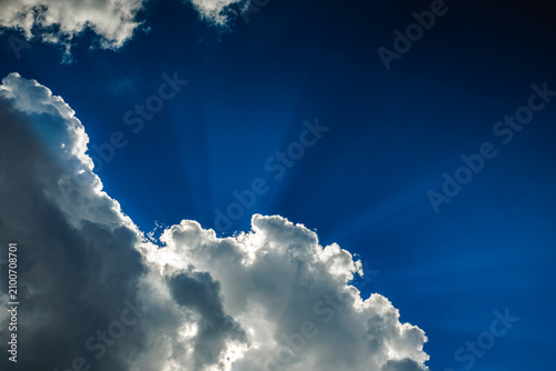 Dramatic blue sky with sun rays shining through fluffy white clouds