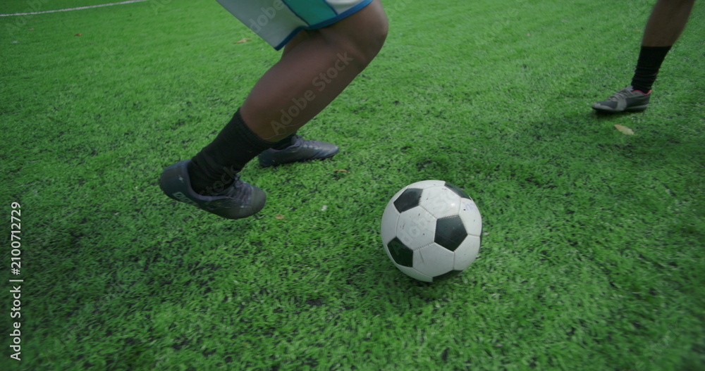 Fototapeta premium Close-up of soccer player running with ball and kicking toward goal during friendly community game, showing movement, coordination, and teamwork on sunny urban field