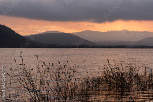 Φωτογραφία Dawn light reflects on lake with distant hills and reeds in foreground